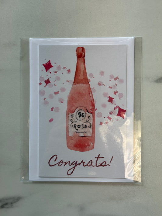 Greeting card with a bottle of 90 Rose and 'Congrats!' text on a marble surface.
