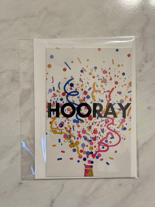 Greeting card with 'HOORAY' text and colorful confetti design on a marble surface