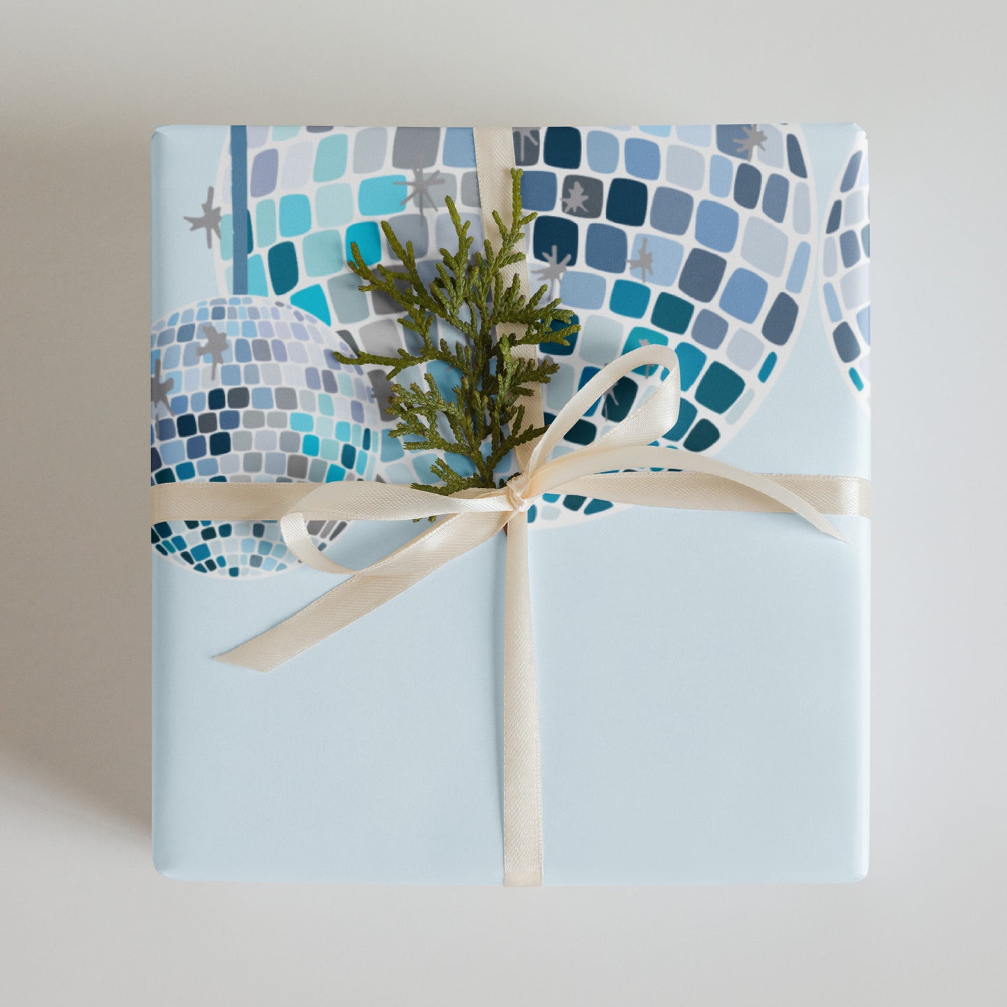Gift wrapped in blue mosaic paper with a green plant and beige ribbon on a light gray background