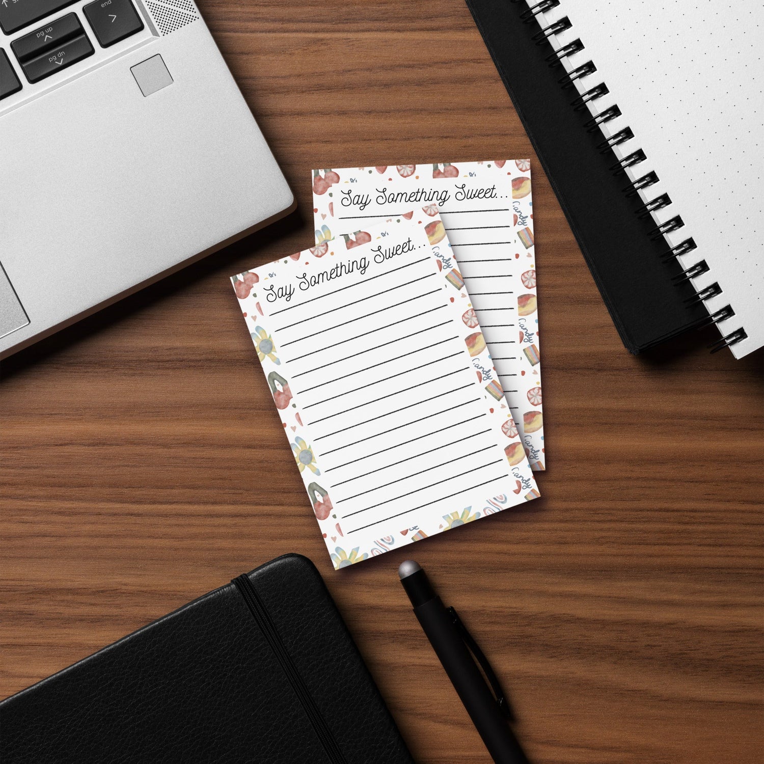 "Hand-drawn 'Say Something Sweet' lined notepad stationery on a wooden desk next to a laptop and black notebook from Wishbrush"