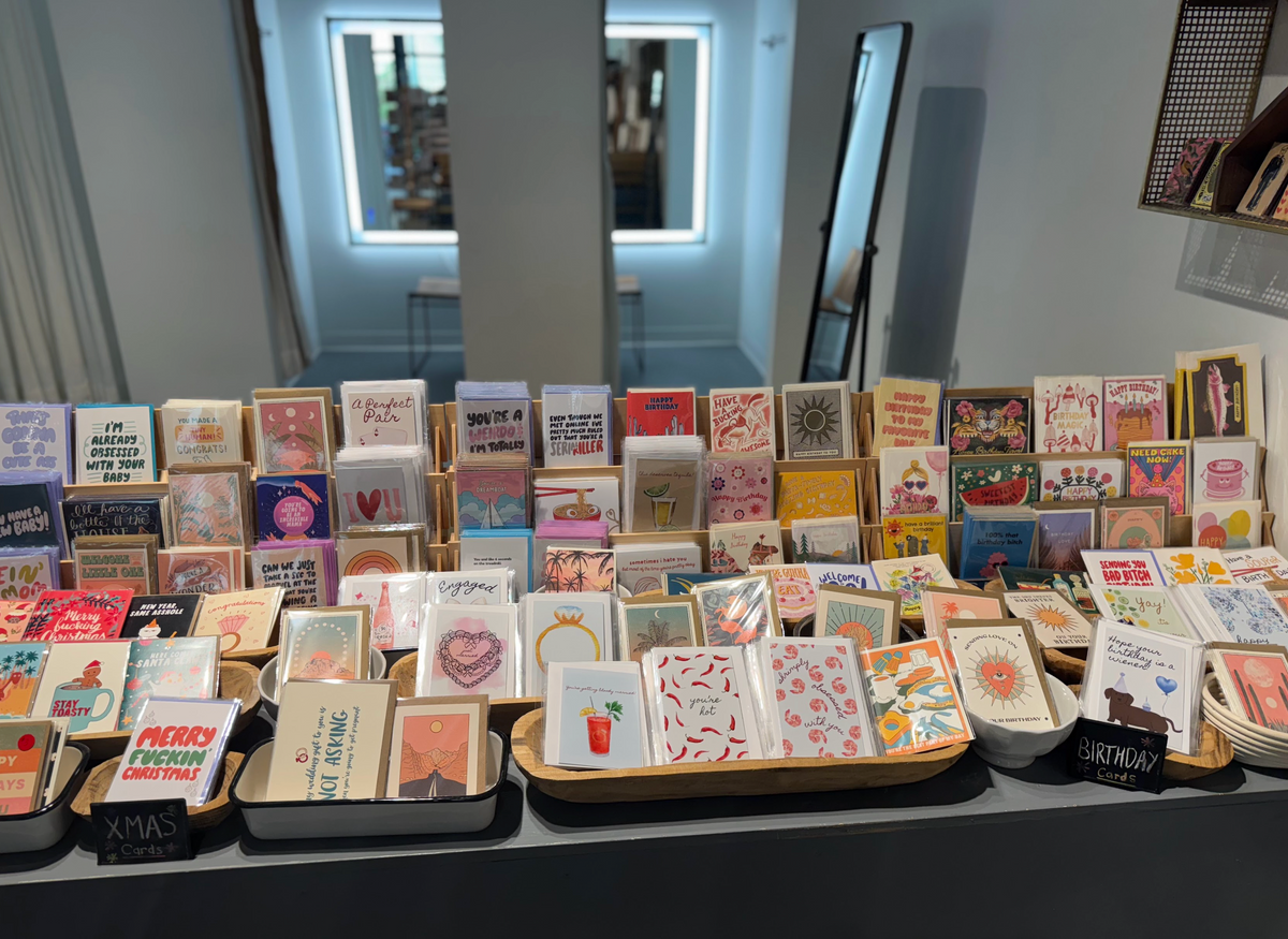 Display table filled with colorful greeting cards organized in wooden and ceramic trays inside a retail shop.