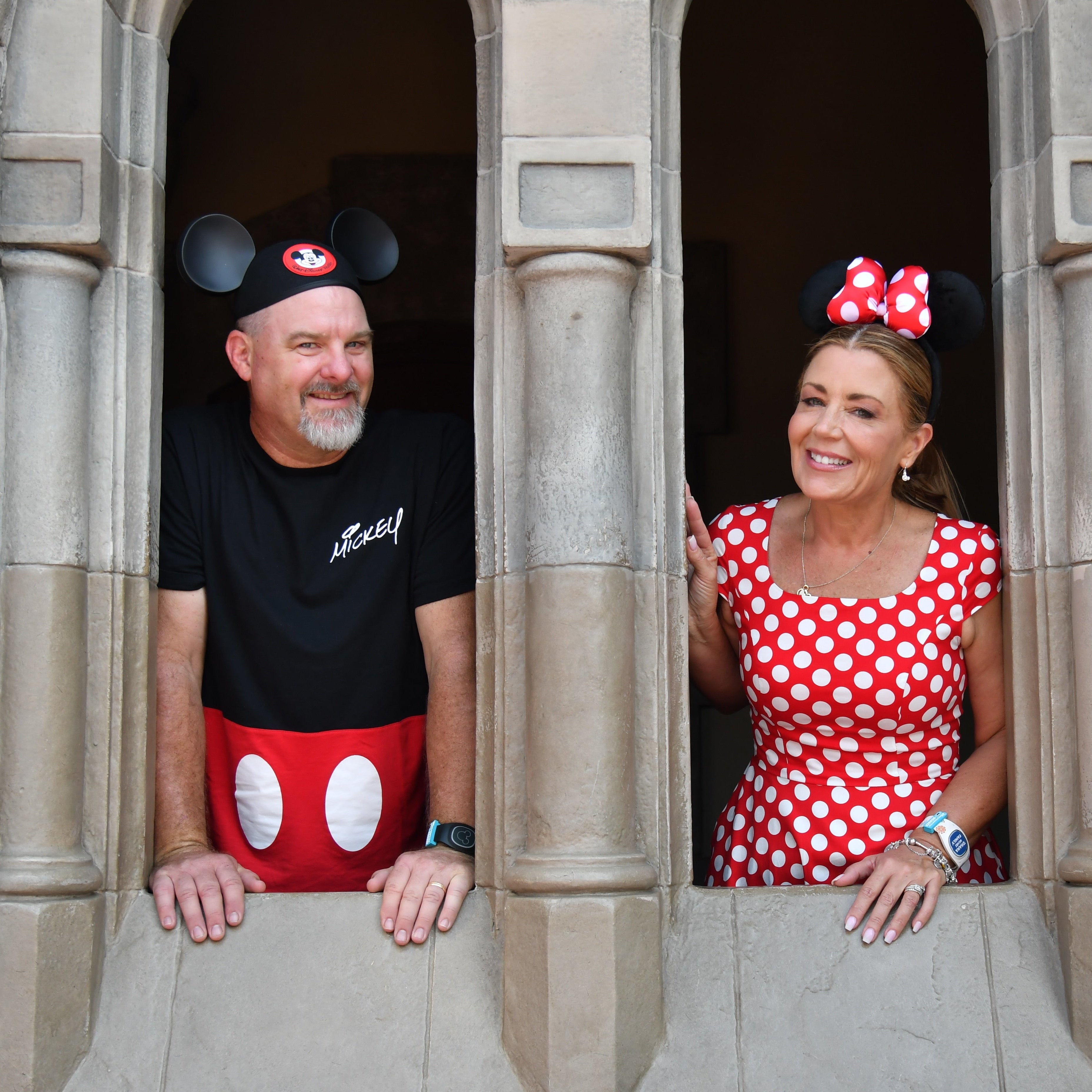 Two people wearing Mickey and Minnie Mouse ears standing in a stone wall.
