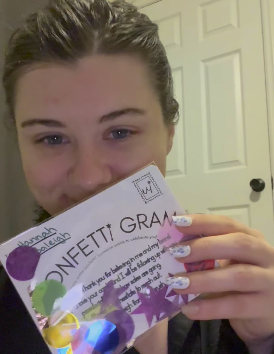 Person holding a card with 'Confetti Gram' text in front of a white door.