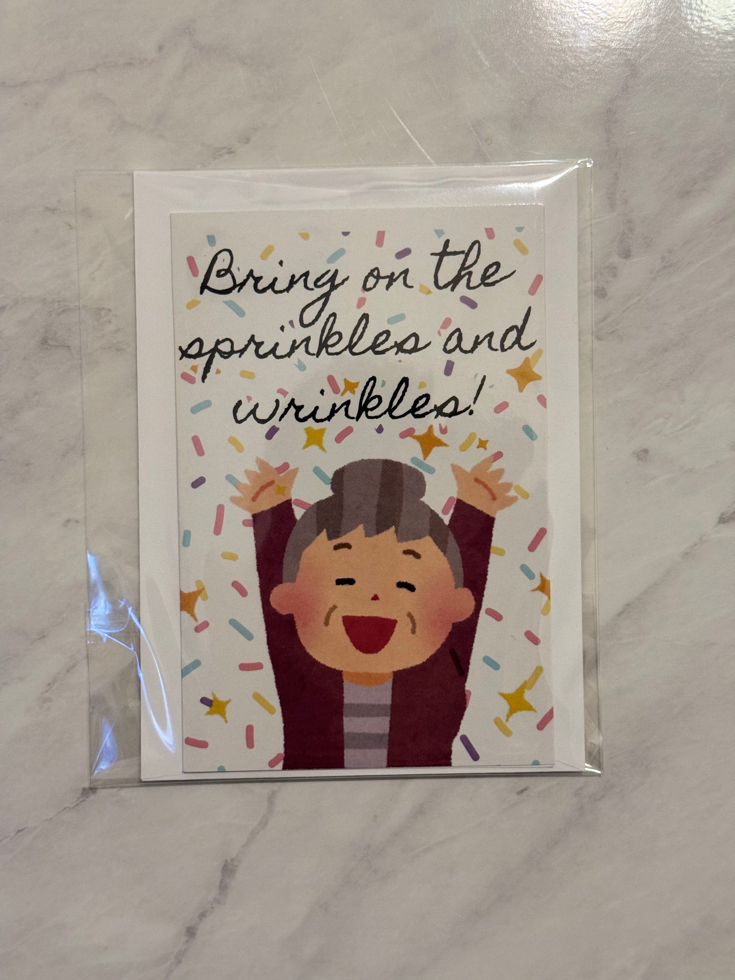Card with a child illustration and text 'Bring on the sprinkles and wrinkles' on a marble surface.