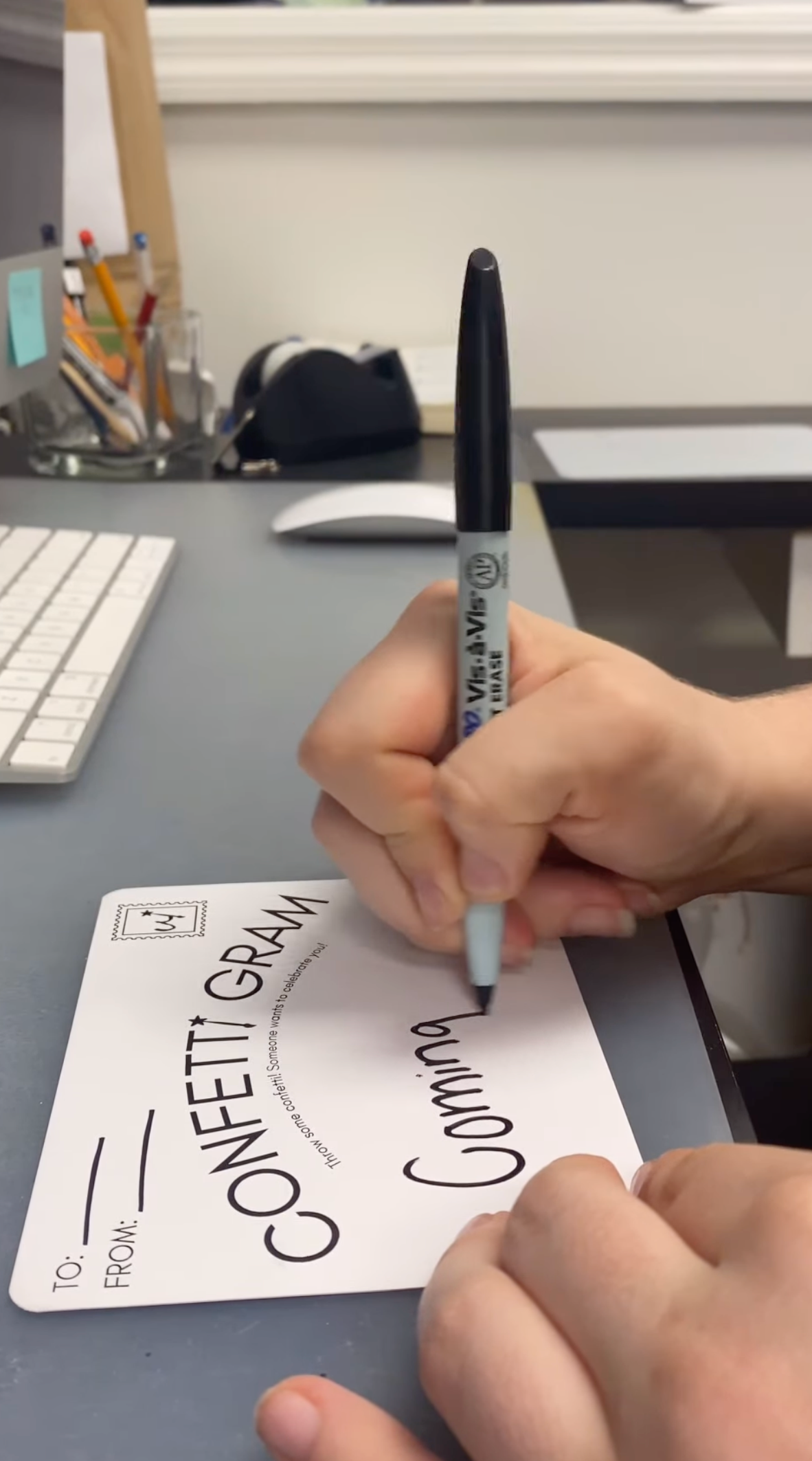 Hand writing on a card with a pen, desk in the background