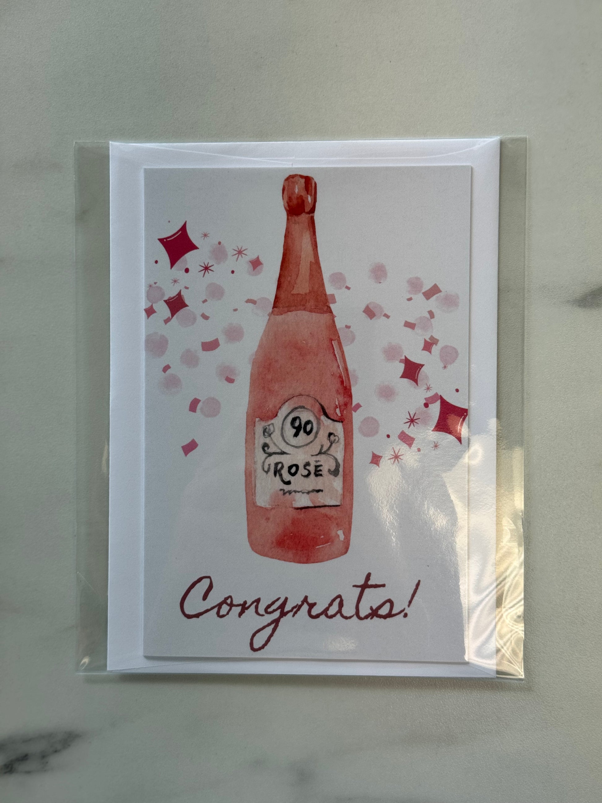 Greeting card with a bottle of 90 Rose and 'Congrats!' text on a marble surface.