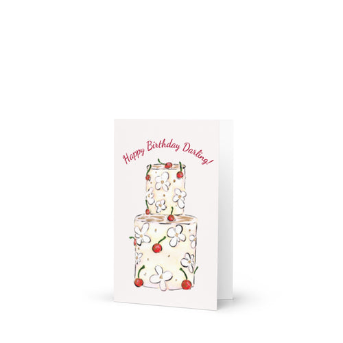 A vertical greeting card with a white background featuring an illustration of a two-tiered cake decorated with white flowers and red cherries. The text 'Happy Birthday Darling!' is written in red cursive above the cake.