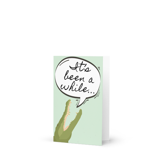 Greeting card with a crocodile and speech bubble saying 'It's been a while' on a light green background