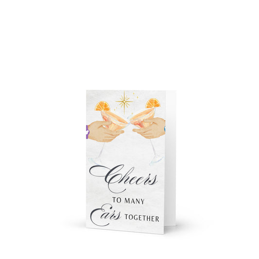 Greeting card with illustration of two hands holding champagne glasses and text 'Cheers to Many Ears Together' on a white background.