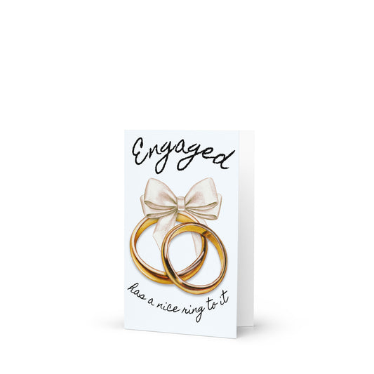 Greeting card with two gold rings and a bow, featuring the text 'Engaged has a nice ring to it' on a white background.