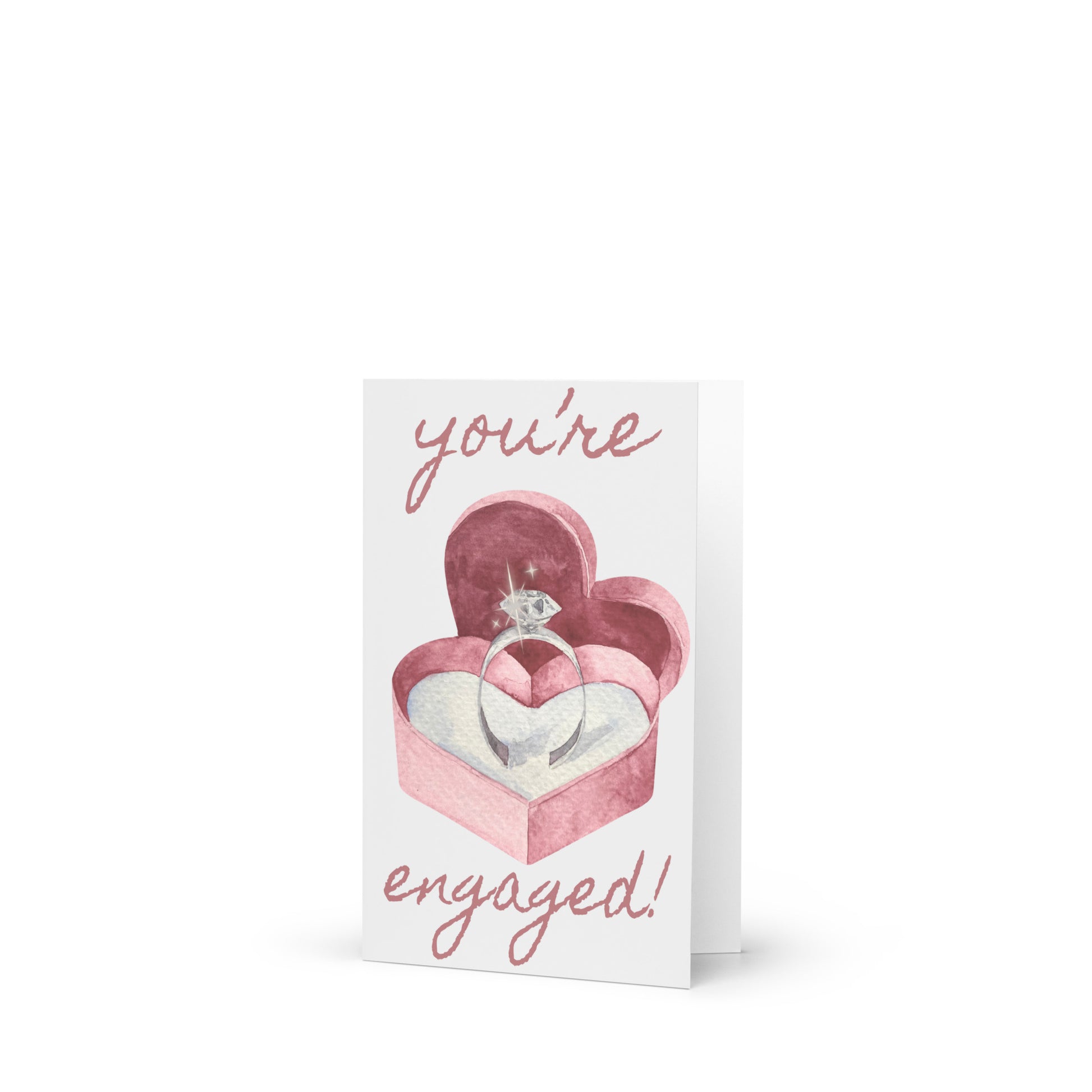 Greeting card with a heart-shaped box containing an engagement ring and 'you're engaged!' text on a white background.