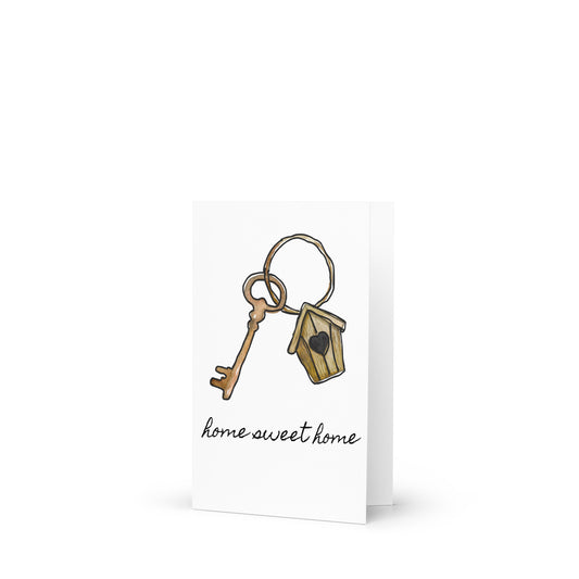 Greeting card with key and birdhouse charm and 'home sweet home' text on a white background