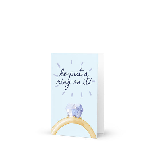 Greeting card with a ring holder and 'he put a ring on it!' text on a light blue background
