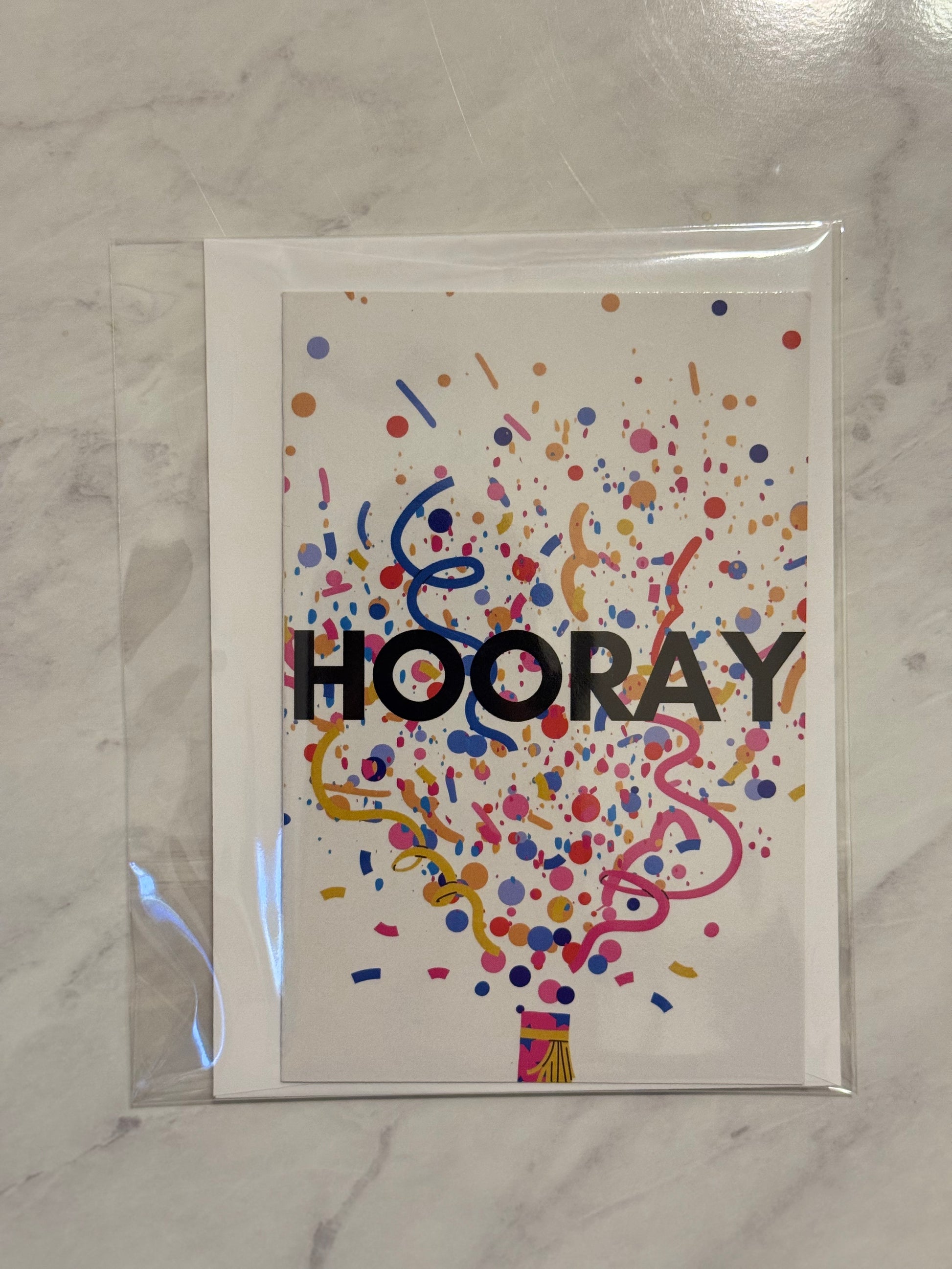 Greeting card with 'HOORAY' text and colorful confetti design on a marble surface