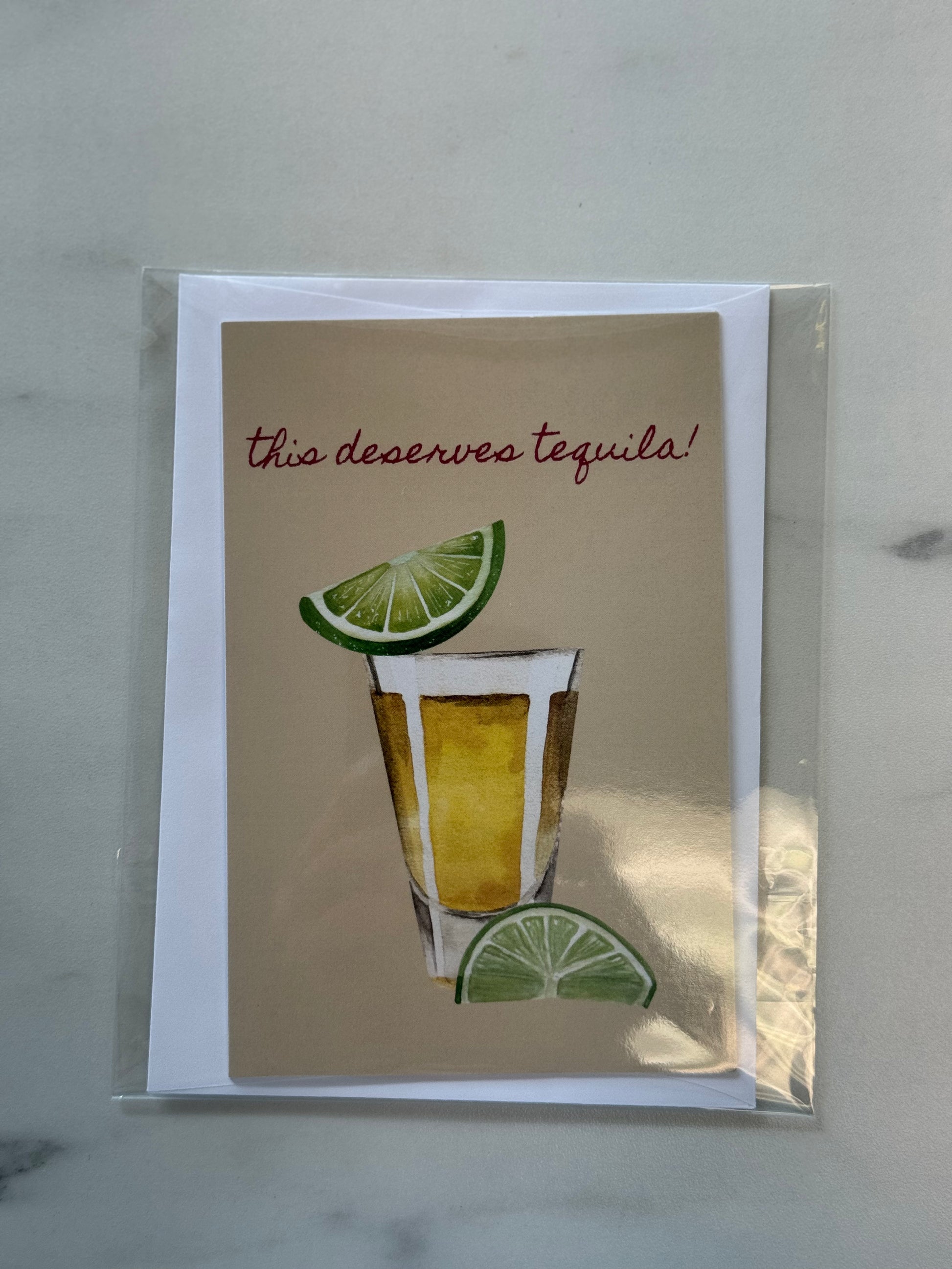 Card with a shot glass and lime garnish, text 'this deserves tequila!', on a beige background.