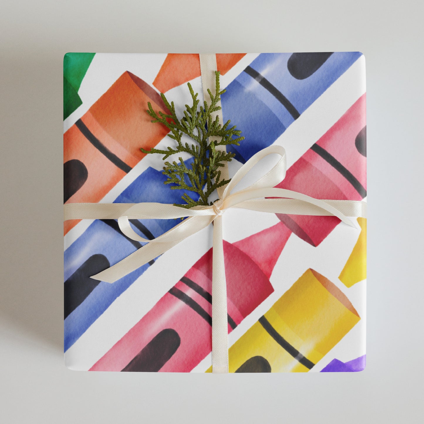 Colorful crayons-patterned gift box with a white ribbon and greenery on a neutral background