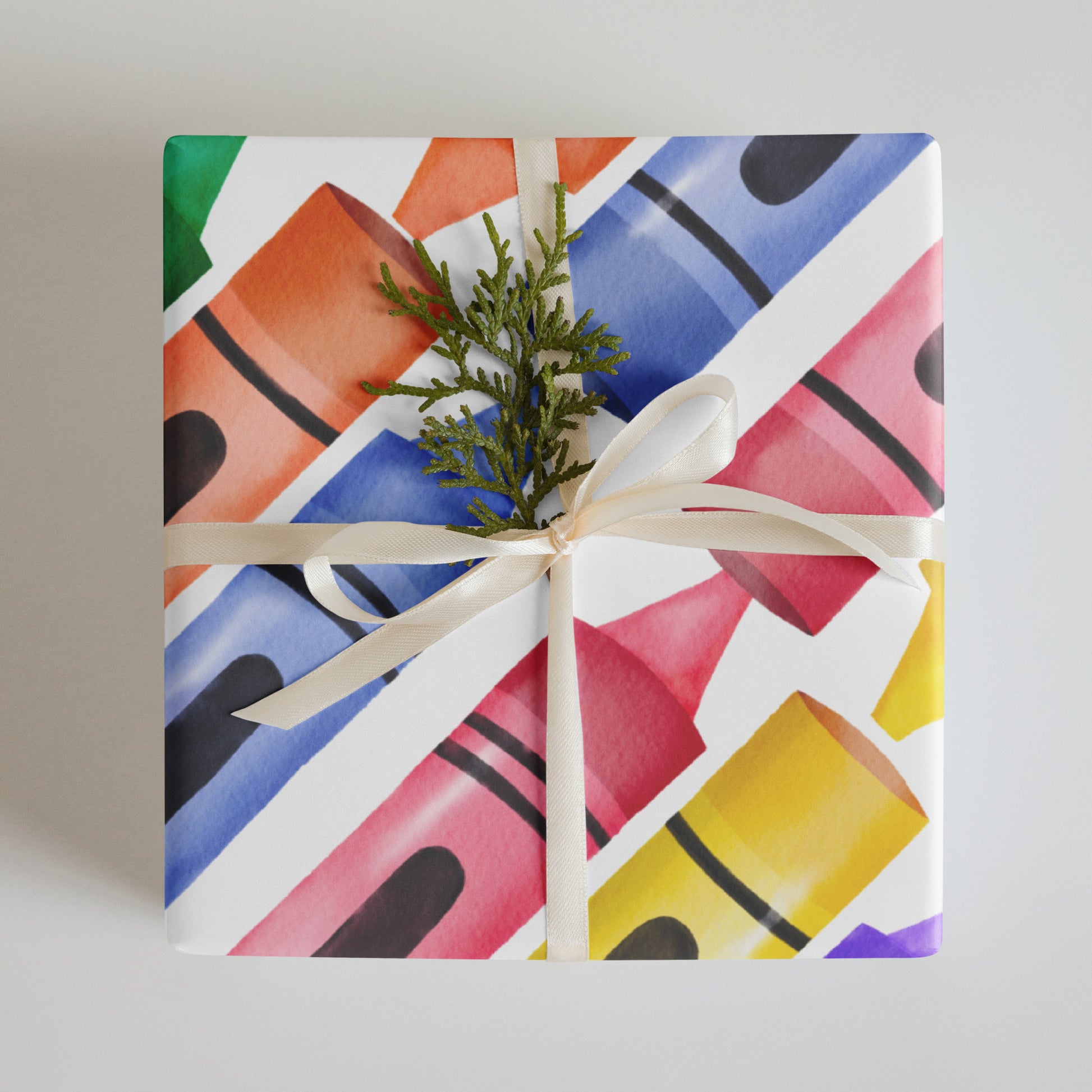 Colorful crayons-patterned gift box with a white ribbon and greenery on a neutral background
