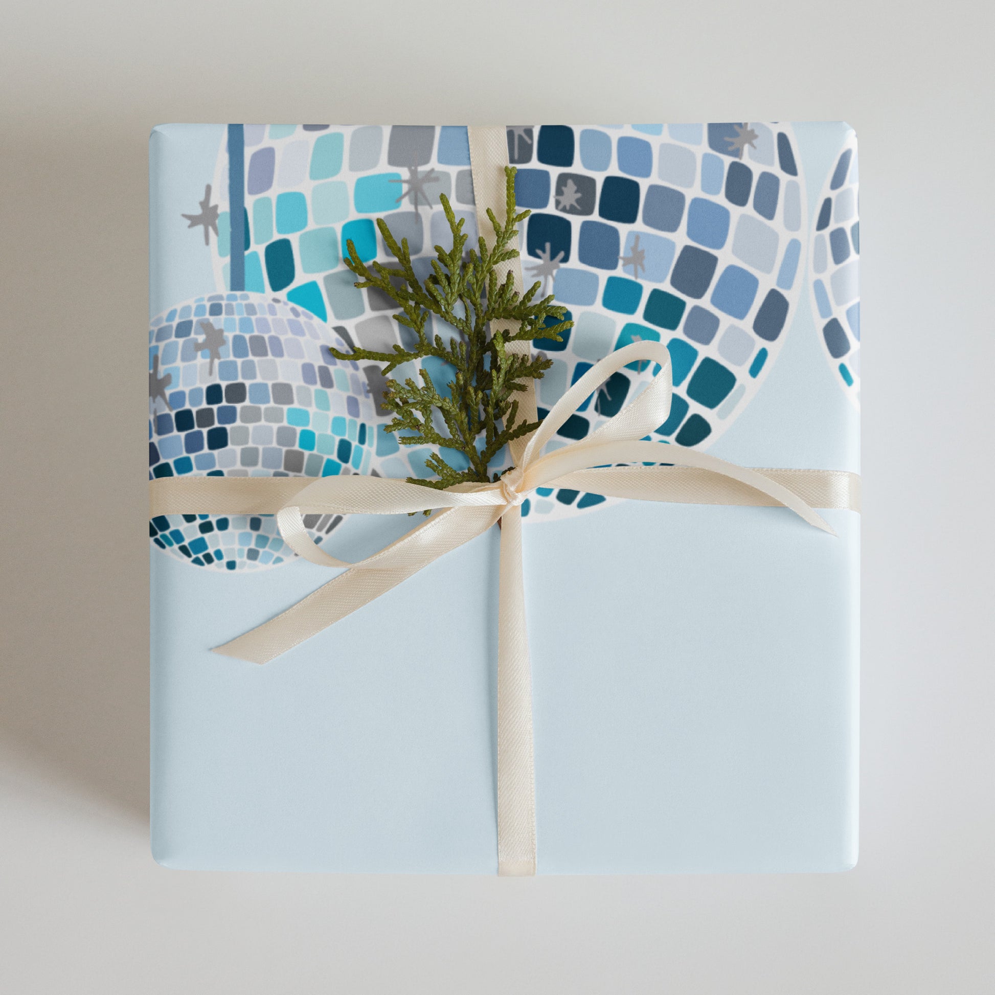 Gift wrapped in blue mosaic paper with a green plant and beige ribbon on a light gray background