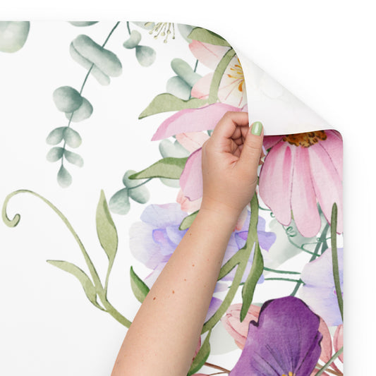 Hand peeling back a floral sticker sheet with pink and purple flowers on a white background