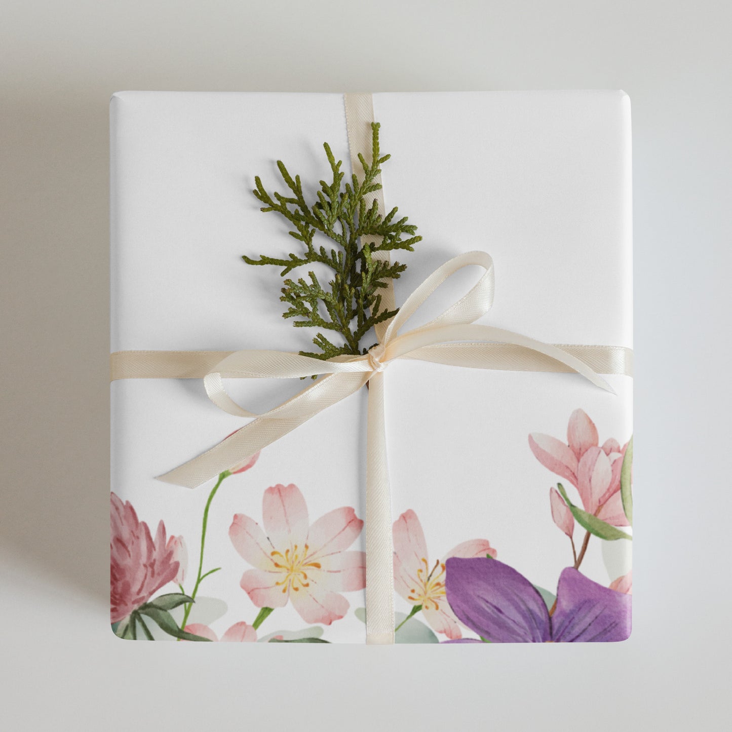 Gift wrapped in floral paper with a green branch and beige ribbon on a light background
