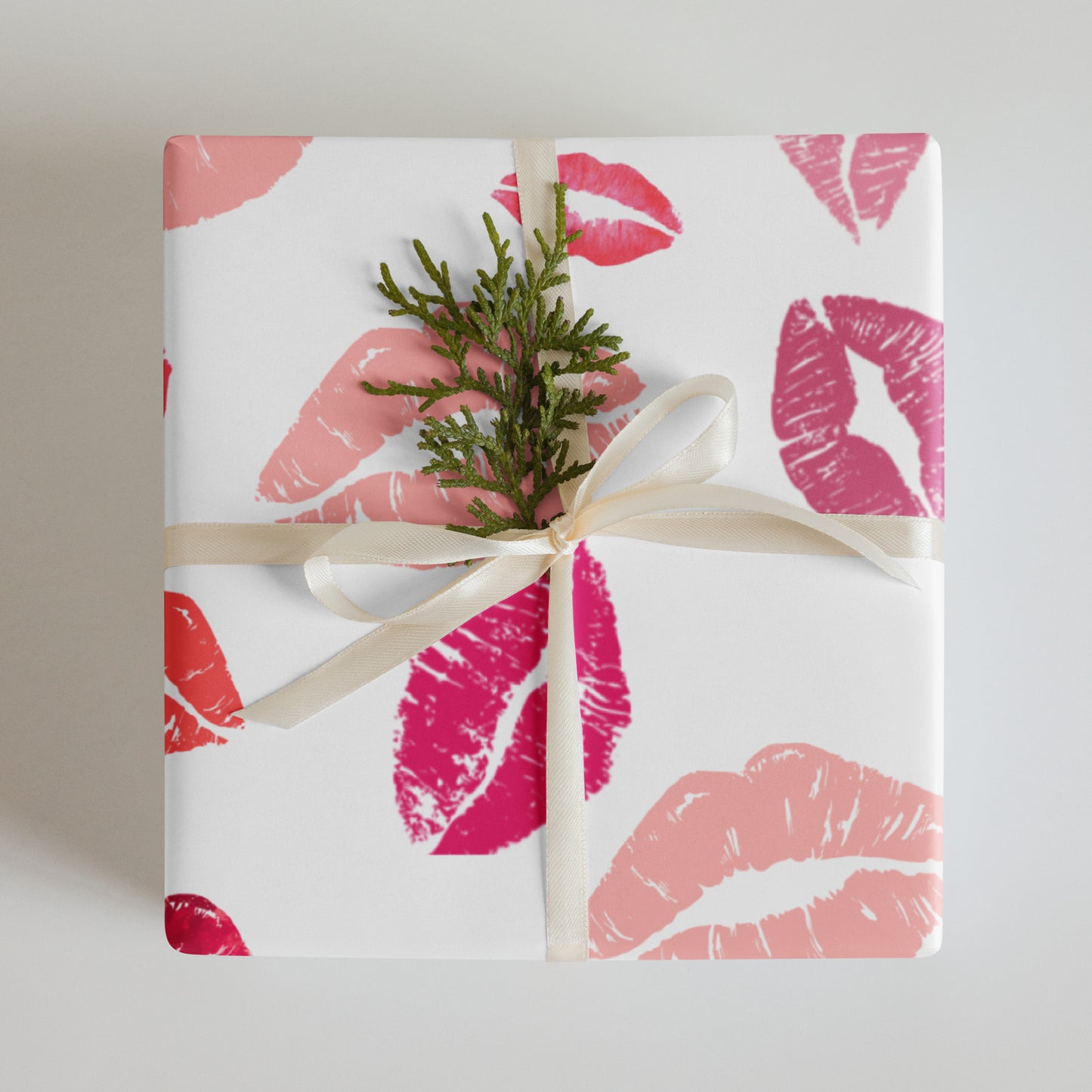Gift wrapped in paper with pink lip prints and a sprig of greenery on a neutral background
