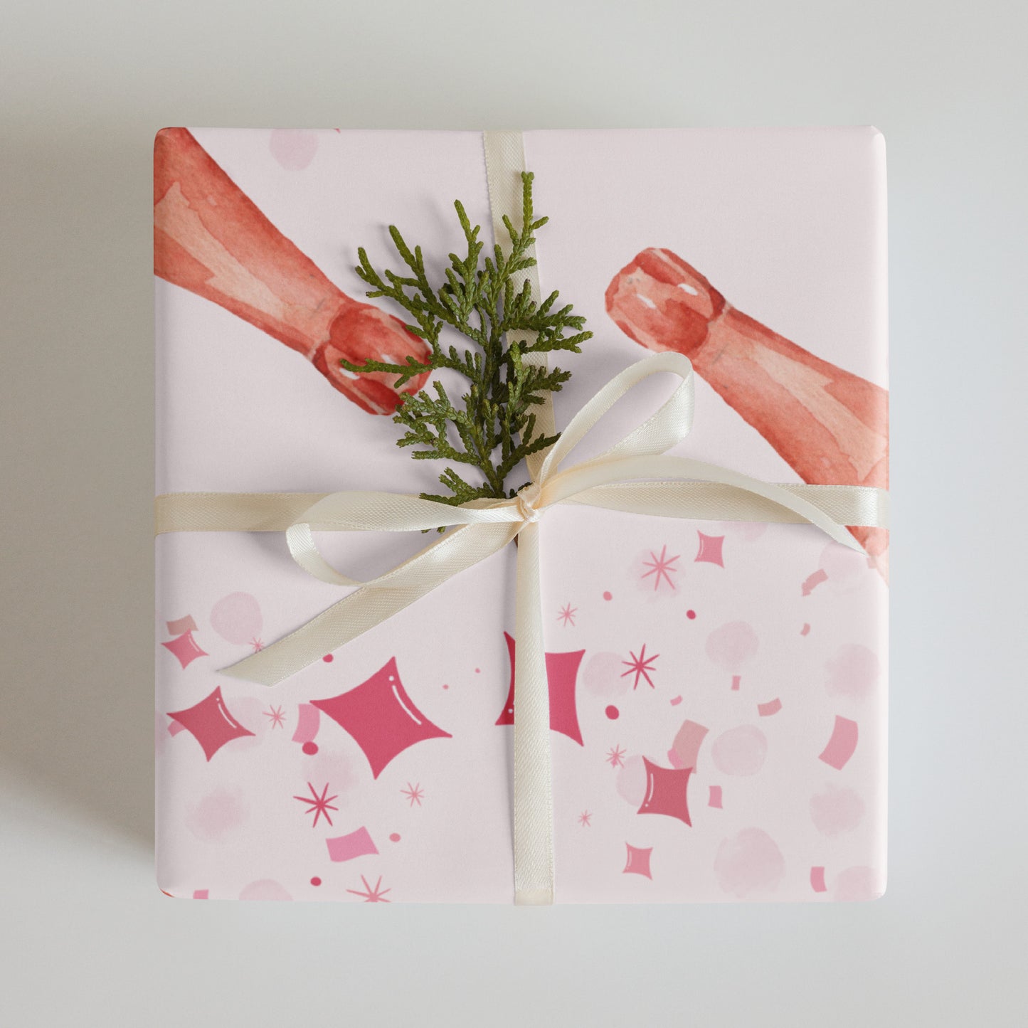 Gift wrapped in pink and white patterned paper with a green branch and white ribbon on a light gray background
