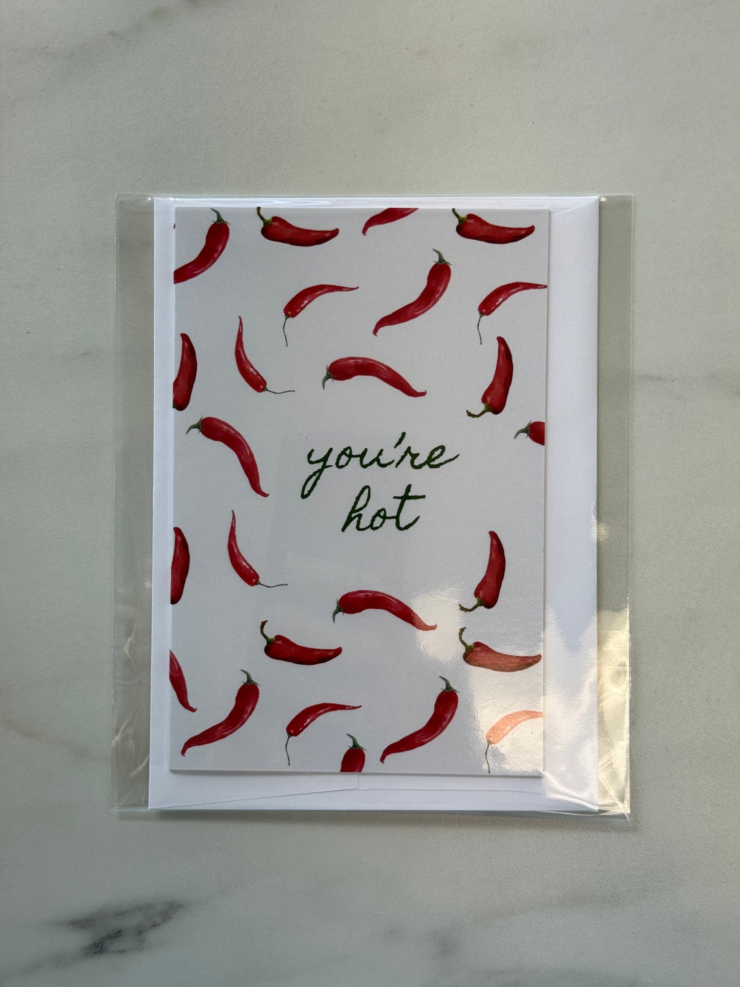 Card with red chili pepper pattern and 'you're hot' text on a marble surface