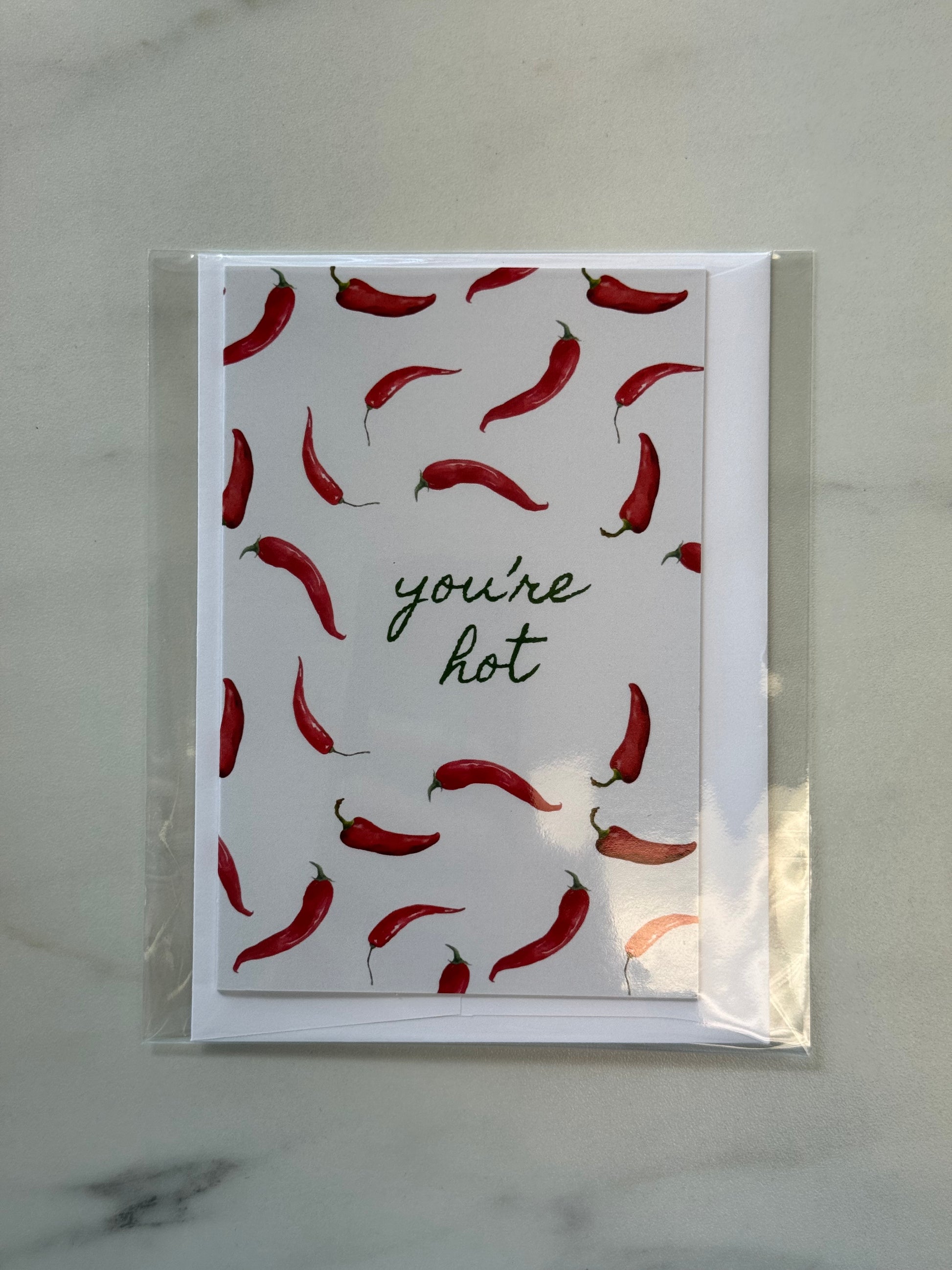 Card with red chili pepper pattern and 'you're hot' text on a marble surface